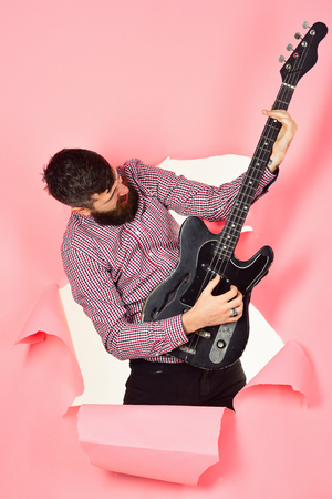 Guitarist through hole in pink paper hold guitar in hand. Bearded man, guitarist with electric guitar. Hobby, music instrument, education, entertainment, concert and learning concept. Music instrumentの写真素材