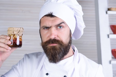 Serious bearded chef holds jar with honey nuts. Professional chef buys best groceries in grocery...