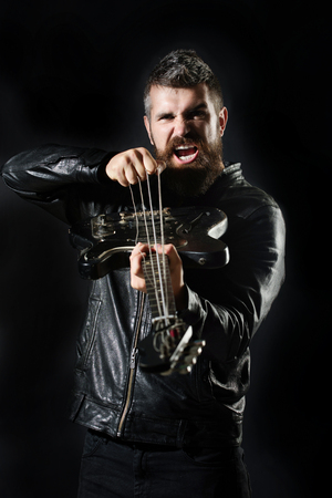 Bearded man with electric guitar. Guitarist in black leather jacket stands with bass guitar....