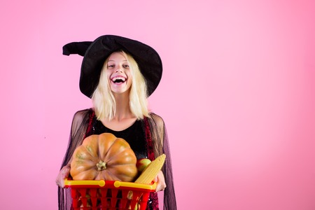 Halloween shopping. Halloween witch hold grocery shopping basket with food. Happy woman holds shopping basket with groceries. Woman at store with shopping basket. Sale. Discount. Copy space for store.の写真素材