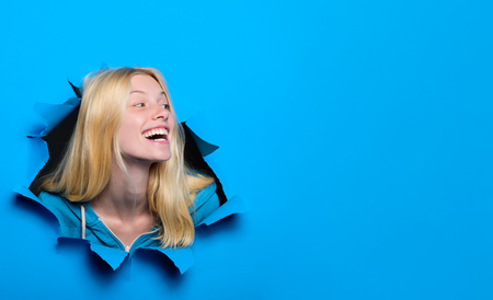 Happy blonde girl looking through hole in paper. Woman breaking through paper wall. Emotions. Emotional woman breaking through paper. Season sales. Discount, sale. Black friday shopping. Advertising.の写真素材