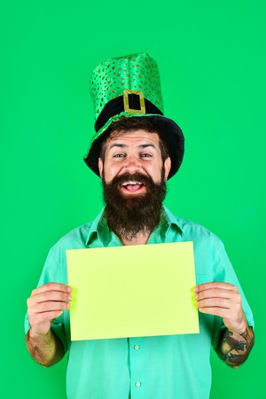 Saint Patrick's Day. Bearded man in green top hat holds green board. St Patrick's Day. Happy four leafed clover. Green hat with clover. Ireland tradition. Copy space. Sale. Discount. Advertising.の写真素材