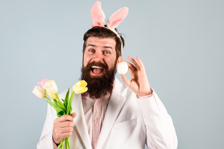 Bearded man in suit hold egg&bouquet tulips. Rabbit man in bunny mask with flower. Happy Easter. Preparation for Easter. Spring holiday. Spring flower. Easter bunny costume. Easter celebration conceptの写真素材