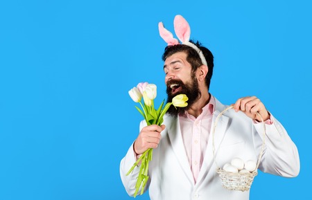 Bearded man in suit holds basket with eggs. Rabbit man in bunny mask with flower. Happy Easter....