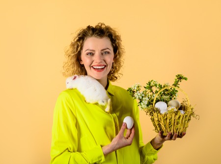 Easter girl with bunny and basket with eggs. Happy Easter girl with basket Easter eggs&little rabbit. Girl with eggs in basket. Easter hunt. Smiling woman holds little white rabbit. Spring holidays.の写真素材