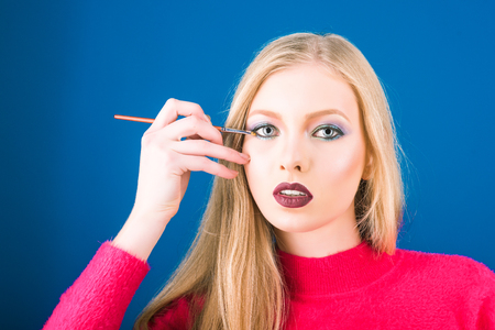 Cosmetics, beauty, makeup, skincare and skin health concept - attractive blonde sexy girl with perfect makeup, dark red lips, clean skin, healthy shiny hair holds brush for makeup near eye.の写真素材