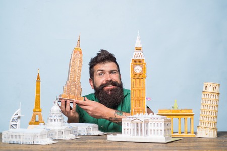 Miniature buildings illustrating travel. Travel concept - happy bearded man holds model Empire State...