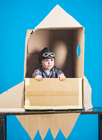 Boy play with rocket. Childhood concept. Kid in toy cardboard rocket. Childhood dream. Astronaut. Cosmonaut concept. Space. Isolated on blue background.の写真素材