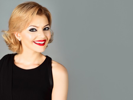Portrait of blonde girl with evening makeup on gray background. Beautiful makeup and black dress. Skin and face care. Jewelry and Beauty. Blonde girl in black evening dress. Copy space for advertisingの写真素材