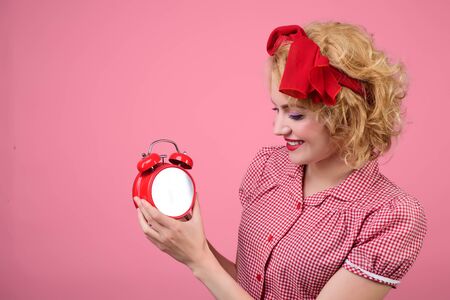 Good morning.Time concept. Attractive glamour girl is looking at clock. Keep track of time. Beautiful fashion pin-up woman with alarm clock. Retro style.Blond pinup woman with alarm-clock in red dressの写真素材