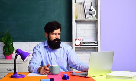 Serious male teacher in school. Learning and education concept. Teachers day - knowledge and educational school concept. Young bearded teacher near chalkboard in classroom.の写真素材