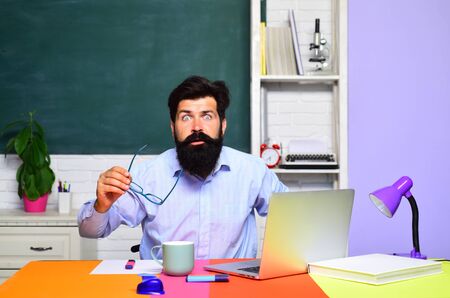 Male student thinks about coursework in university. Teacher in classroom. Students and tutoring education concept. Male student over green chalkboard background. Teachers day. Young serious student.の写真素材