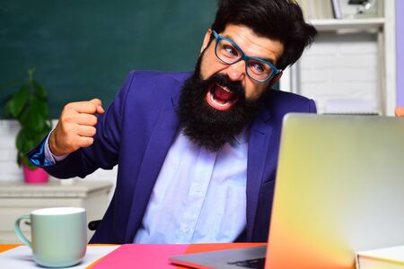 Angry scientist with laptop. Bearded man with notebook. College teacher screaming on students.の写真素材