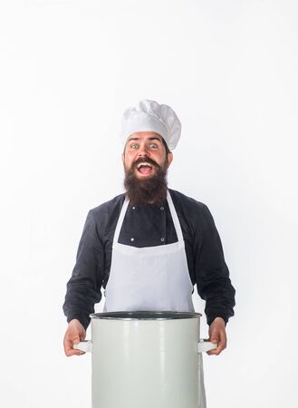 Cook in chef uniform holds saucepan. Male chef. Kitchen utensils concept. Chef in white apron with casserole or saucepan. Cook in white hat and apron holds soup pot. Cuisine, cooking, food preparationの写真素材