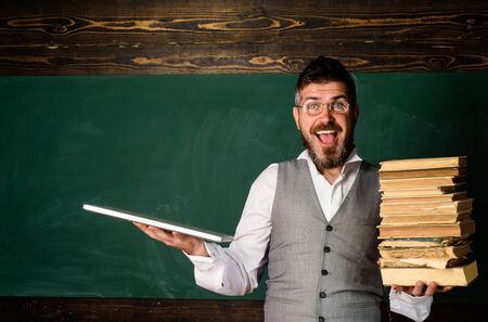 Education, technology, e-learning. Male teacher holds book and laptop. Paper book against laptop. Modern technologies benefit. Online education and learning. Take advantage technologies development.の写真素材