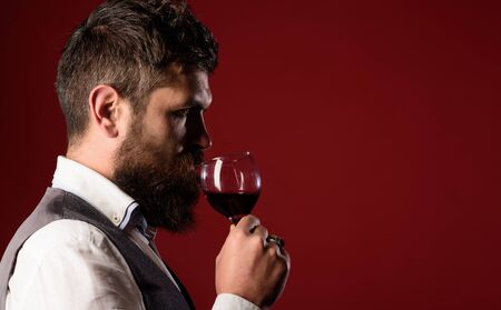 Wine tasting and degustation concept. Sommelier tasting red wine. Handsome businessman is drinking red wine with enjoyment. Man in waistcoat holds glass of red wine. Bearded man tasting glass of wine.の写真素材