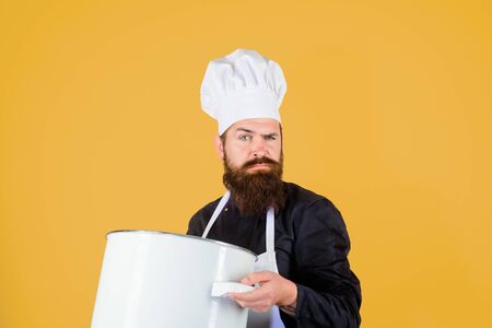 Cook man in apron holds saucepan in kitchen. Cookware, dinnerware, kitchenware. Cooking pot, saucepan, casserole. Cooking, culinary, food, profession and people concept - male chef cook holds big pot.の写真素材