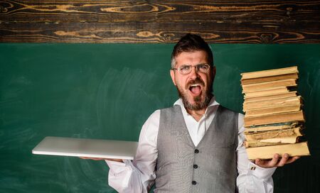 Serious teacher holds books and laptop. Reading digital copy. Online education, e-learning. Male student with books and notebook. Electronic library, e-book concept. Electronic education with laptop.の写真素材