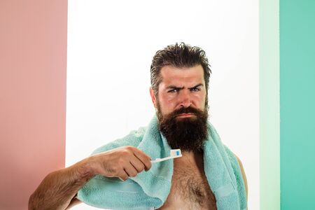 Oral care. Bearded man brushing teeth with toothbrush. Dental hygiene. Handsome man cleaning teeth in bathroom. Serious young man with toothbrush cleaning teeth. Morning routine of washing teeth.の写真素材