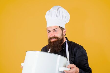 Male chef cook holds saucepan. Cookware, tool, kitchenware. Professional cookery concept. Cook preparing food in restaurant kitchen. Chef cooking food in saucepan. Chief chef with saucepan in kitchen.の写真素材