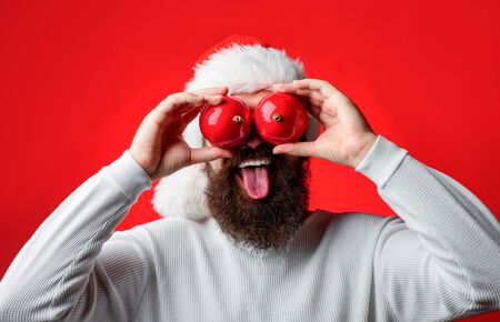 Santa shows tongue. Happy Santa hold christmas balls. Bearded man holds Christmas toy near eyes.の写真素材