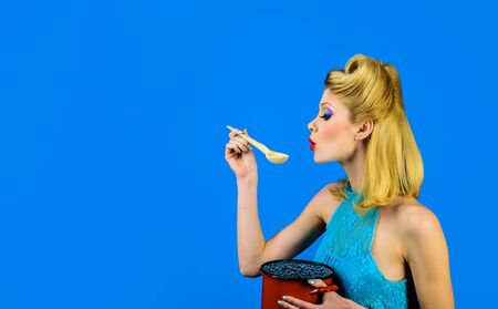 Retro woman cooking in kitchen. Pretty girl in vintage style. Pin up housewife tasting soup with pot...