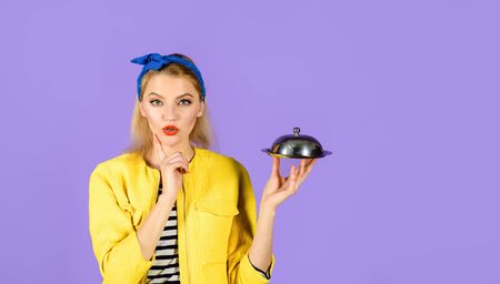 Thoughtful woman holds food tray in restaurant. Woman in yellow jacket with cloche food. Retro girl with metal tray with lid. Pinup girl hold metallic dish. Presentation. Restaurant serving.Copy spaceの写真素材