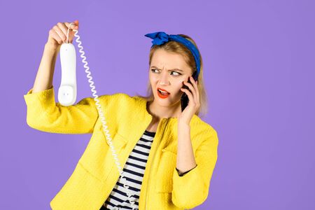 Technological evolution. Phones of different generations. Stylish woman holds wired phone&cell phone. Pin up woman in headband holds handset&smartphone. Pinup girl with retro telephone&mobile phone.の写真素材