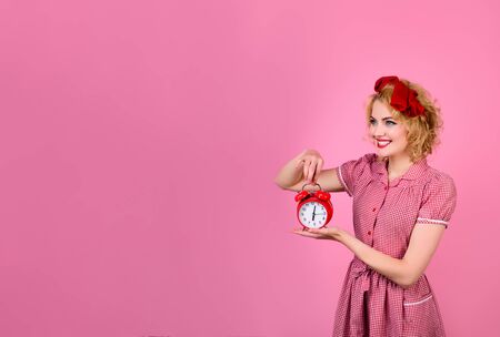 Beautiful blond girl holds retro alarm clock. Happy smiling pinup woman showing alarm clock. Saving time concept. Black friday. Shopping time. Season sales. Discount. Business time management concept.の写真素材