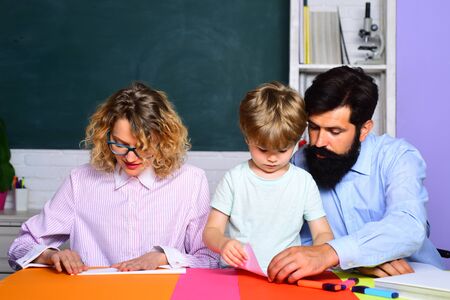 Mom and dad helps his son. Cute pupil and his parents making paper airplane. Education. Educational process. Cheerful family playing with set for creativity. Home schooling. Origami lesson. Parenting.の写真素材
