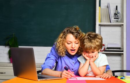 Mom helping her little child with homework. Happy family. Mum and son together painting using marker. Schoolboy drawing at home with his mother. Mother and son drawing together. First time to schoolの写真素材