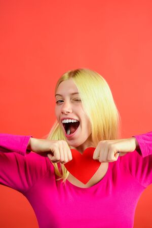 Romantic mood, Valentine's Day concept. Beautiful woman holds Valentines day paper heart card. Emotions, feeling, flirtation. Winking cheerful woman holds romantic symbol. Love time. Valentine heart.の写真素材