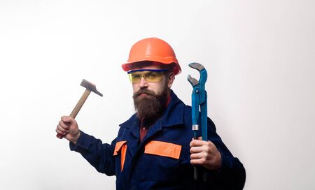 Bearded man with repair tools in hand. Repair service. Worker in helmet with pipe wrench. Bearded...