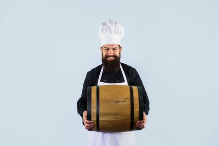 Brewer in apron holds barrel with craft beer at brewery factory. Bearded man seller in uniform with...