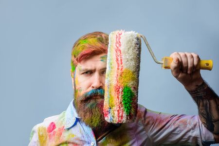 Painter. Bearded painter with paint roller in front of face. Painter with painting roller covered...