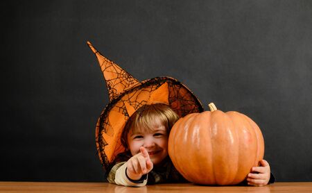 Little boy in witch hat with halloween pumpkin pointing to you. Boy dressed up trick or treating....