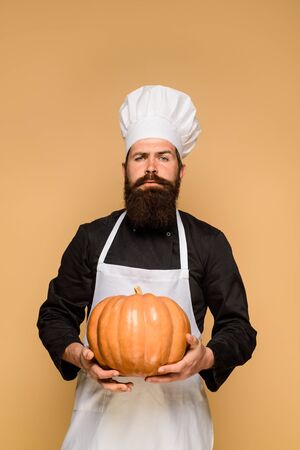 Chef man with pumpkin. Male chef in uniform with pumpkin. Bearded man hold squash. Organic food. Happy halloween. Healthy product. Harvest festival. Thanksgiving day cooking or autumn recipes conceptの写真素材
