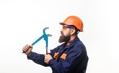 Bearded worker with tools in hand. Repair tools. Repair service. Worker in helmet with pipe wrench. Bearded man in construction helmet. Uniform. Mechanic. Plumbing and renovation.の写真素材