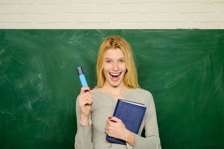 Teacher. Portrait of young smiling teacher in classroom. Young professor educates students. Teacher with marker. Portrait of female teacher with book near chalkboard.の写真素材