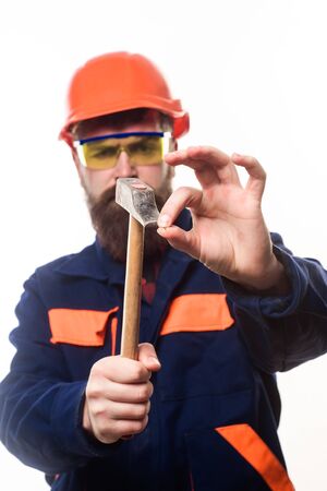 Builder, master clogs nail. Repairman using hammer clogs nail. Bearded man clogs nail with hammer. Carpenter with hammer. Man clogs small nail. Repair service. Builder in hard hat. Selective focus.の写真素材