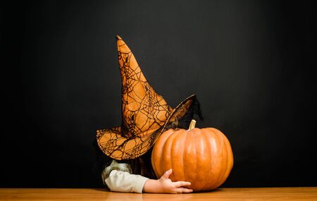 Jack o lantern. Little boy in witch hat hiding at halloween pumpkin. Preparation for Halloween...