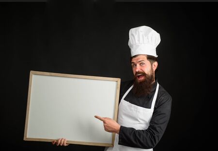 Professional chef on kitchen. Empty menu chalkboard with copy space for text. Master chef, baker or cook shows menu sign blackboard. Cooking, culinary, diet, advertisement and food concept. Chef menuの写真素材