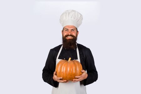 Happy halloween. Useful vegetables. Autumn crop. Seasonal vitamin. Happy chef man with beard holds pumpkin. Thanksgiving day cooking. Autumn recipes concept. Bearded man cook in chef hat with pumpkinの写真素材
