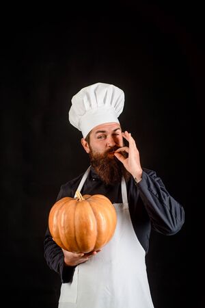 Seasonal vitamin. Autumn recipes concept. Happy halloween. Thanksgiving day cooking. Useful vegetables. Autumn crop. Happy chef man with beard holds pumpkin. Bearded man cook in chef hat with pumpkinの写真素材