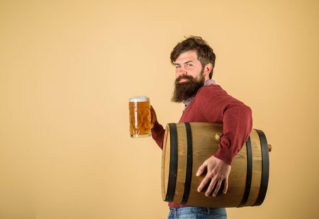 Beer time. Bearded man hold glass and barrel with craft beer. Oktoberfest festival. Attractive bearded brewer with wooden barrel of beer and mug of beer. Holliday, drinks, alcohol and leisure conceptの写真素材