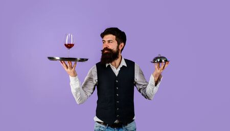 Handsome man waiter in uniform at restaurant. Waiter holds tray with wine and metal cloche lid cover. First class service concept. Best service. Professional catering service. Butler concept. Waiterの写真素材