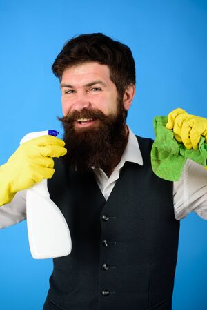 Professional cleaning man in uniform. Bearded man in uniform, rubber gloves with cleaning products. Domestic service cleaner man with rag and cleaner spray. Male janitor with cleaning equipmentsの写真素材