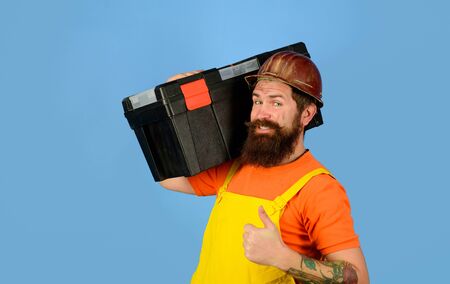 Repairman in overall hold toolbox giving thumbs up. Man with tool box. Builder in protective helmet...