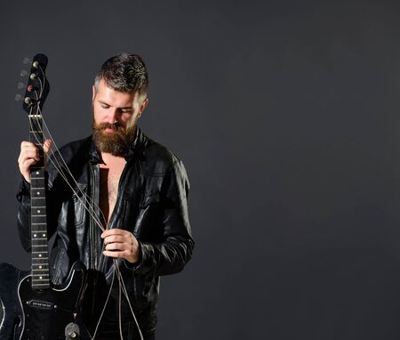 Handsome bearded in leather jacket with electric guitar. Man with beard holds musical instrument. Guitarist in jacket with electric bass guitar. Music party, entertainment. Rock musician with guitarの写真素材