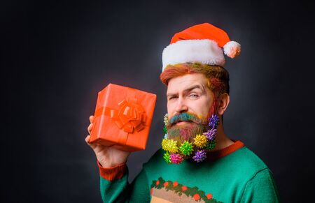 Merry Christmas. Santa Claus holds present. Bearded man in santa hat with decorated beard for New Year holiday. Christmas beard decorations. Santa Claus man hold Christmas gift. Christmas decorationの写真素材